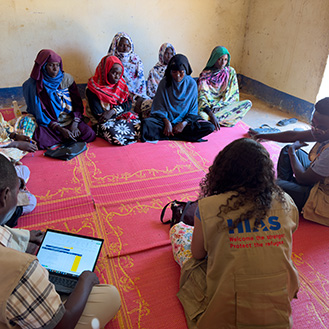 HIAS workers sitting on the floors with women in need. Links to What to Give